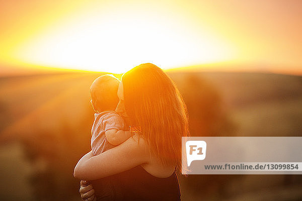 Seitenansicht einer Mutter  die ihr Kind bei Sonnenuntergang trägt