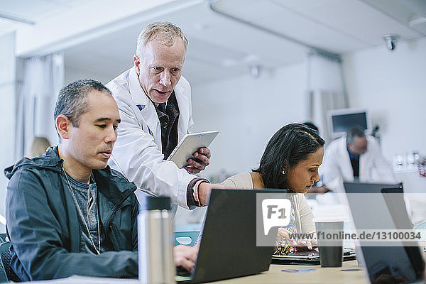 Männlicher Arzt diskutiert mit Kollegen über Laptop-Computer im Behandlungszimmer