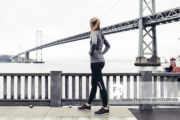 Seitenansicht einer Athletin  die auf die Oakland Bay Bridge schaut  während sie auf einem Fußweg steht