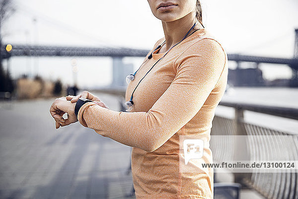 Seitenansicht einer Sportlerin  die auf dem Fußweg eine smarte Uhr trägt  mit der Williamsburg-Brücke im Hintergrund