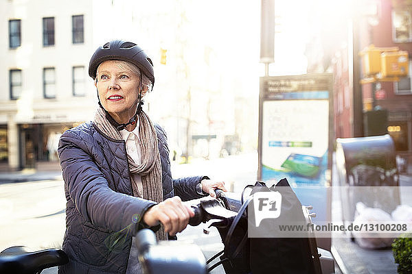 Nachdenkliche ältere Frau sitzt auf dem Fahrrad auf der Straße