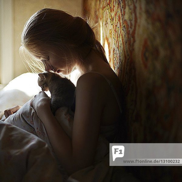 Seitenansicht einer Frau  die mit einer Katze auf dem Bett sitzt