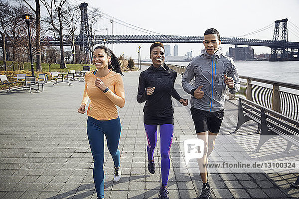 Glückliche multiethnische Athleten laufen auf einem Fußweg mit der Williamsburg-Brücke im Hintergrund