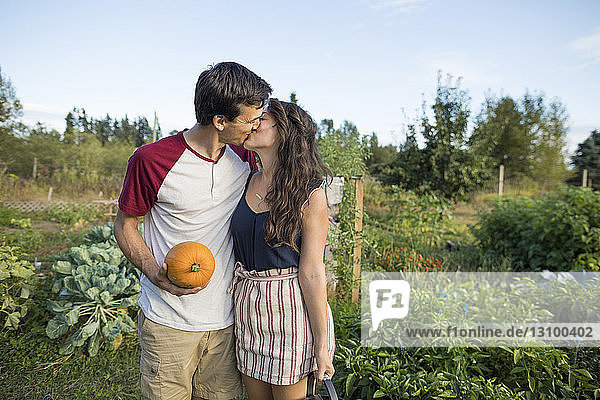 Young couple kissing while standing against sky at community garden