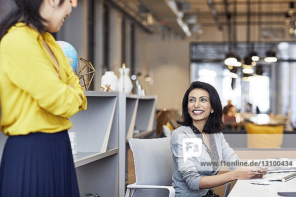 Happy businesswoman looking at female colleague while sitting in creative office