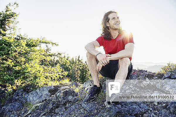 Cheerful hiker sitting on field against clear sky