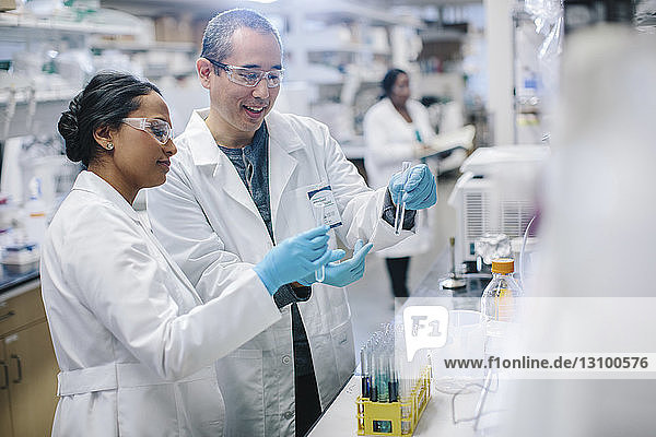 Doctors examining test tubes while coworker working in background at laboratory