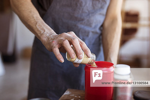 Midsection of senior artist putting powder in container