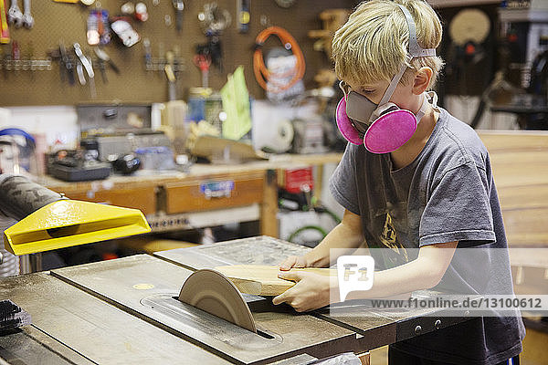 Junge schneidet Holz mit der Tischsäge in der Werkstatt