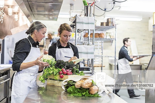 Weibliche Köche untersuchen Gemüse  während ein männlicher Mitarbeiter im Hintergrund arbeitet