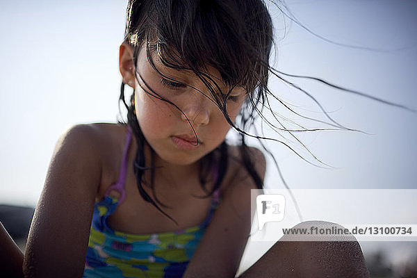 Niedrigwinkelansicht eines Mädchens in Badebekleidung  das bei Sonnenuntergang vor dem klaren Himmel kauert