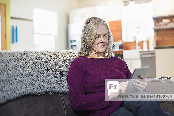 Senior woman using tablet computer while sitting on sofa at home