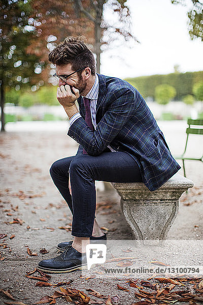 Thoughtful businessman sitting on park bench during autumn