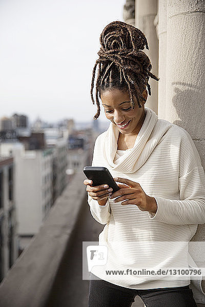 Lächelnde Frau benutzt Smartphone  während sie auf dem Balkon steht