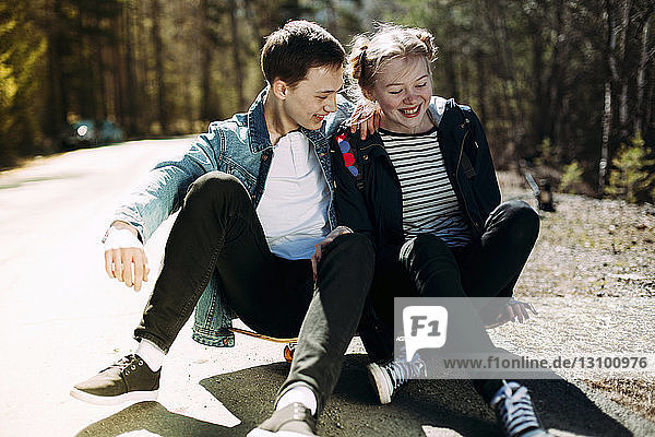 Glückliches Paar sitzt bei strahlendem Sonnenschein auf einem Skateboard