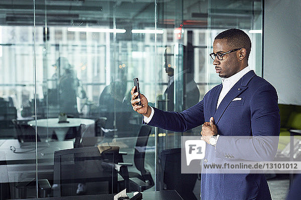 Geschäftsmann schaut auf Smartphone  während er im Büro steht