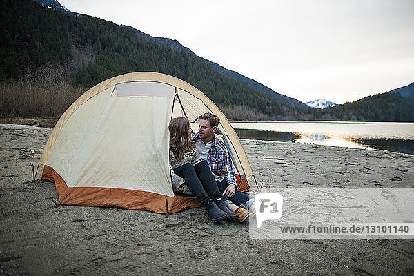 Young couple looking face to face while sitting in tent at lakeshore