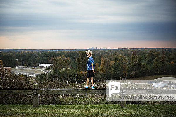 Boy standing on wooden fence against trees
