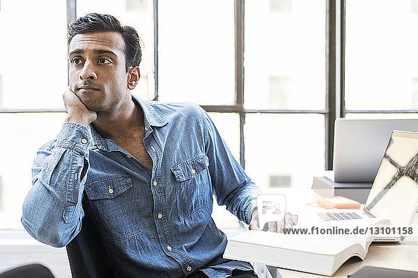 Thoughtful businessman with hand on chin sitting at desk in office