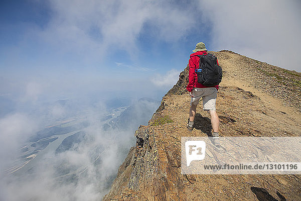 Rear view of hiker with backpack climbing mountain amidst clouds