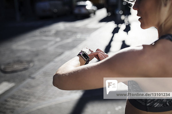 Weibliche Sportlerin schaut auf die Uhr  während sie auf der Straße steht