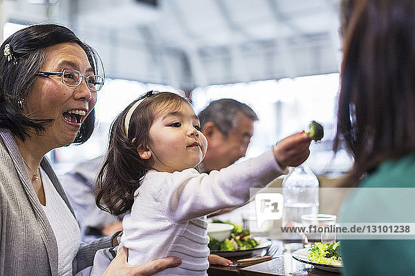 Girl feeding mother while sitting with grandparents at table in restaurant