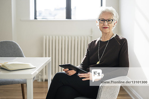 Portrait of businesswoman holding digital tablet and sitting on chair