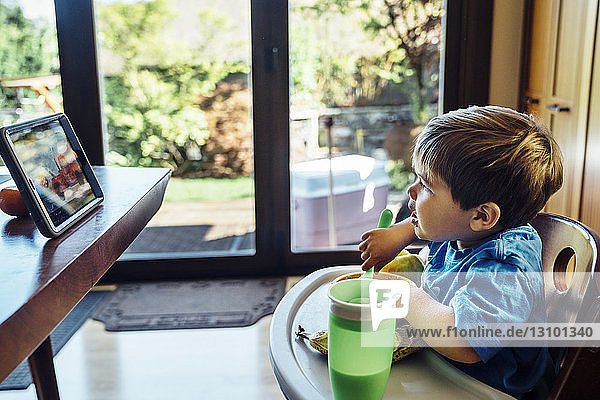 Junge schaut auf digitale Tablette und isst zu Hause