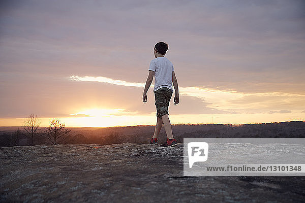 Rückansicht eines Jungen  der bei Sonnenuntergang auf dem Arabien-Berg gegen bewölkten Himmel läuft