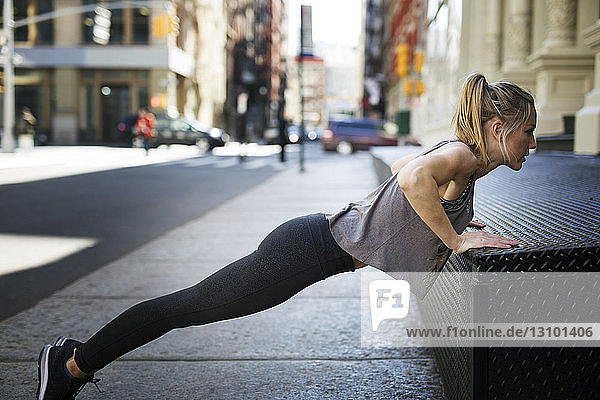 Female athlete doing push-ups at sidewalk in city