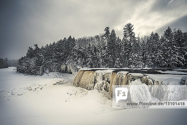 Landschaftliche Ansicht des Wasserfalls vor bewölktem Himmel am Wald im Winter