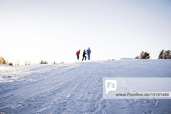 Friends enjoying on snow covered mountain against clear sky