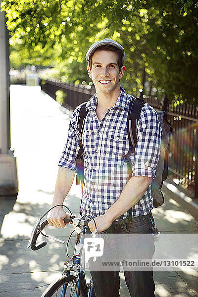 Portrait of happy man holding bicycle and standing on street