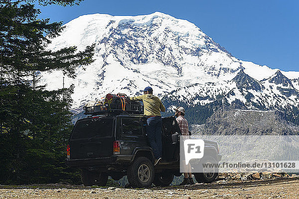 Hiker adjusting luggage on off-road vehicle by friend against snowcapped mountains