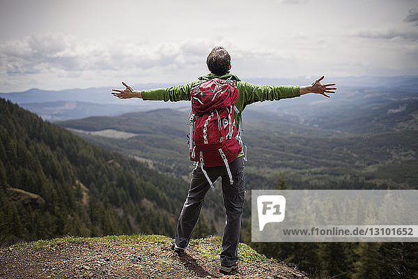 Rear view of man with arms outstretched standing on mountain