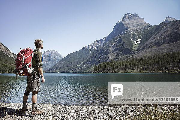 Hiker carrying backpack while standing by lake at Glacier National Park