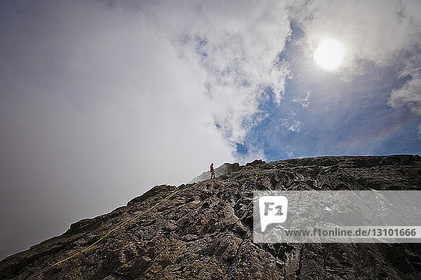 Mitteldistanzansicht eines Wanderers  der an Felsformationen vor bewölktem Himmel klettert