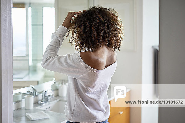 Side view of woman looking in mirror while standing at home