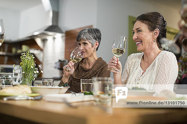Lächelnde Freundinnen  die Wein trinken  während sie bei geselligem Beisammensein am Tisch sitzen