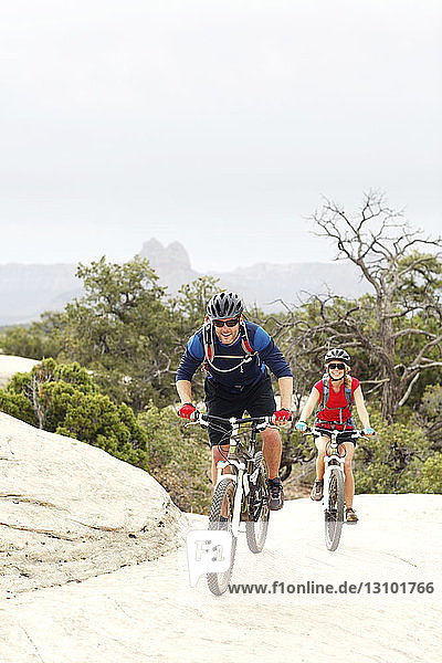 Lächelndes Paar fährt Fahrrad auf Felsen gegen klaren Himmel