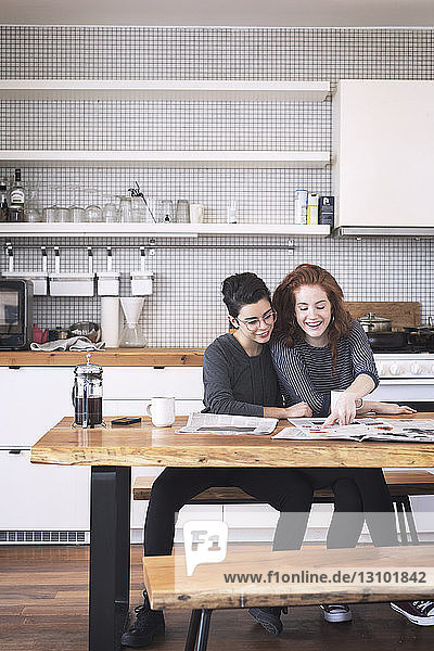 Smiling lesbians couple reading newspaper while sitting at table