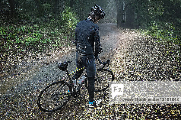 High angle view of man standing with bicycle on dirt road in forest
