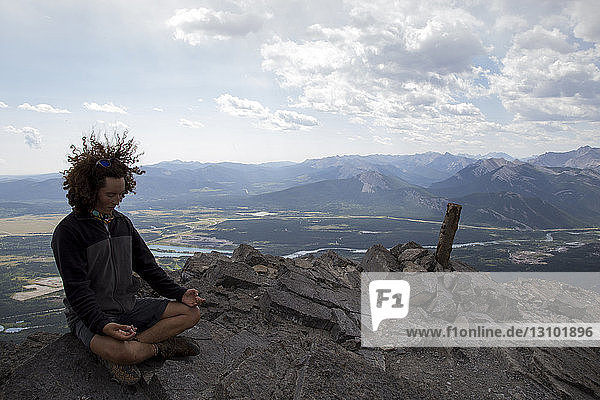 Full length of man meditating while sitting on rock against sky