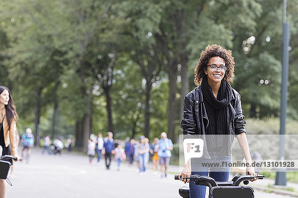 Glückliche Frau fährt Fahrrad mit Freundin im Park