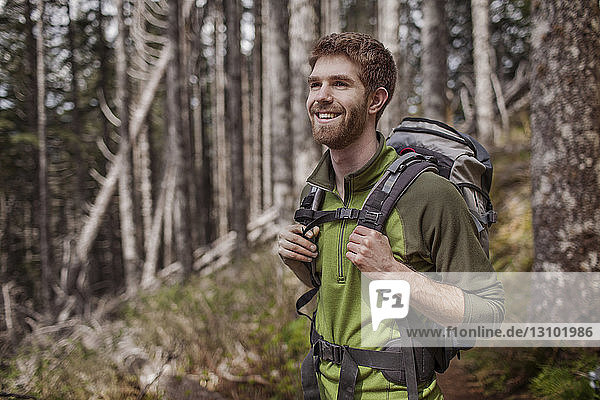 Happy man carrying backpack while standing in forest