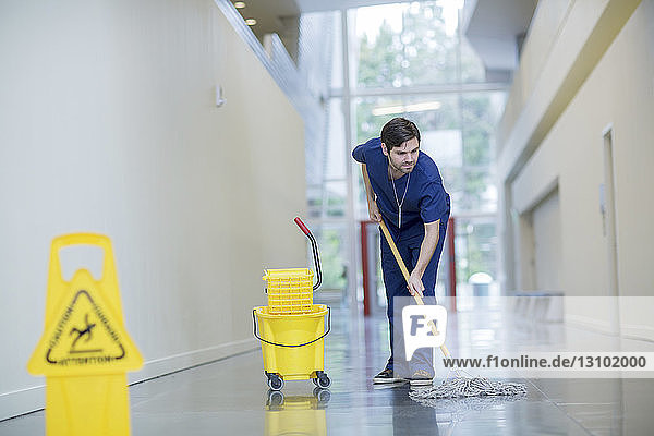 Männlicher Arbeiter reinigt Boden im Krankenhauskorridor