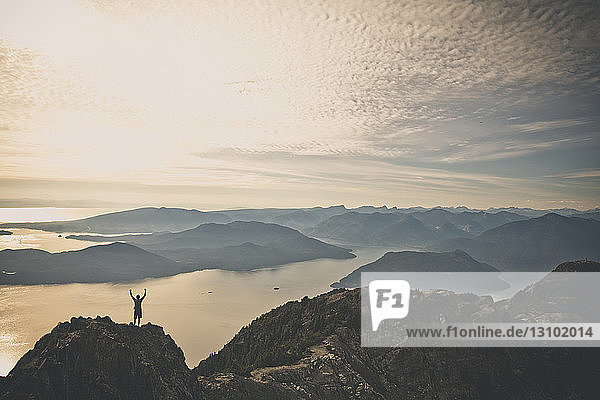 High angle view of hiker with arms raised standing on mountain against cloudy sky during sunset