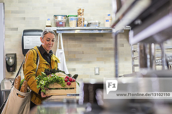 Female chef with crate of vegetables standing at kitchen counter in restaurant