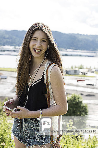 Porträt eines lächelnden Teenager-Mädchens  das auf dem Feld stehend Musik hört
