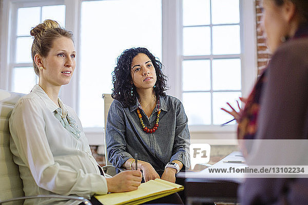 Female colleagues discussing while sitting at desk in office